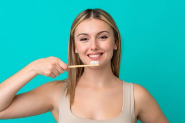 Genç beyaz kadın mavi arka planda izole edilmiş diş fırçası ve mutlu bir ifadeyle.