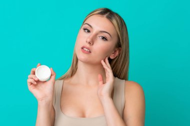 Genç beyaz kadın, mavi arka planda nemlendirici ile izole edilmiş.