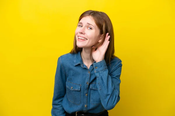 Young English woman isolated on yellow background listening to something by putting hand on the ear