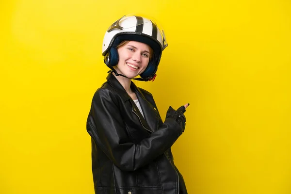 Young English woman with a motorcycle helmet isolated on yellow background pointing back