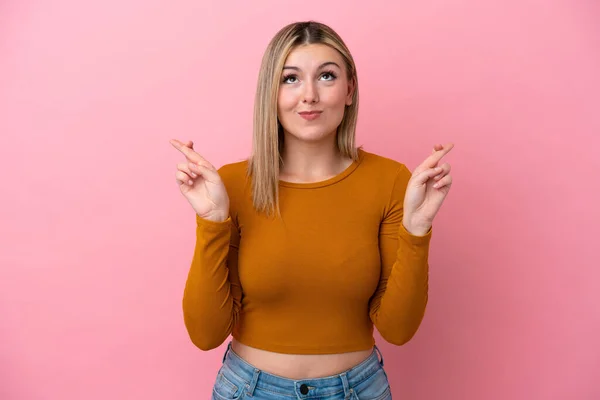 Young caucasian woman isolated on pink background with fingers crossing and wishing the best
