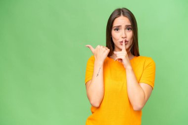 Young pretty caucasian woman over isolated background pointing to the side and doing silence gesture
