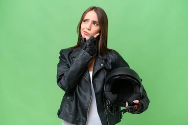 Young pretty caucasian woman with a motorcycle helmet over isolated background having doubts