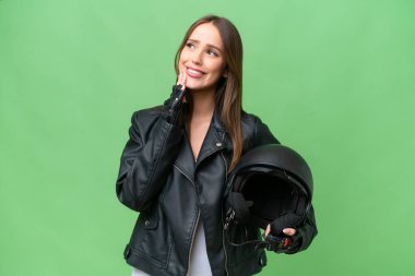 Young pretty caucasian woman with a motorcycle helmet over isolated background looking up while smiling