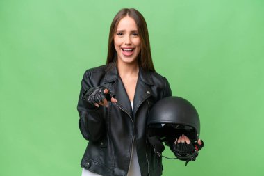Young pretty caucasian woman with a motorcycle helmet over isolated background surprised and pointing front