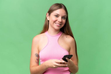 Genç, güzel, sarışın bir kadın izole edilmiş arka planda cep telefonuyla bir mesaj gönderiyor.