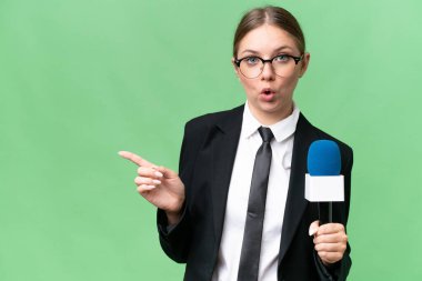 Young TV presenter caucasian woman  over isolated background surprised and pointing side