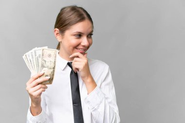 Young business caucasian woman holding money over isolated background thinking an idea and looking side