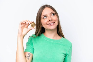 Young beautiful blonde woman holding a Bitcoin isolated on white background looking up while smiling