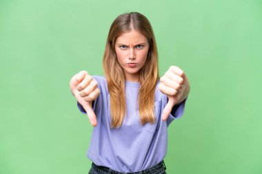 Soyutlanmış arka planda genç ve güzel bir kadın baş parmağını iki eliyle aşağı gösteriyor.