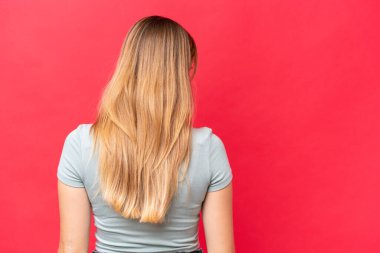 Young beautiful woman isolated on red background in back position and looking side