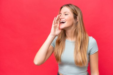 Young beautiful woman isolated on red background shouting with mouth wide open to the side