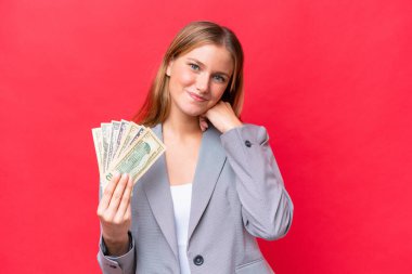 Young business caucasian woman holding money isolated on red background laughing