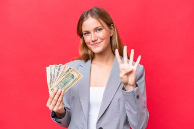 Young business caucasian woman holding money isolated on red background happy and counting four with fingers