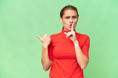 Kafkasyalı genç bir kadın, izole edilmiş arka planda, yan tarafı işaret ediyor ve sessizlik hareketi yapıyor.