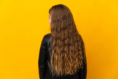 Child over isolated yellow background in back position and looking side