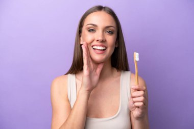 Young caucasian woman brushing teeth isolated on purple background shouting with mouth wide open
