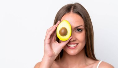 Beyaz arka planda izole edilmiş beyaz bir kadın elinde bir avokado tutarken gülümsüyor. Portreyi kapat