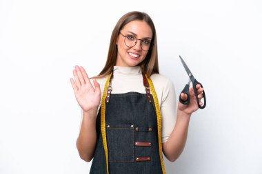 Young seamstress woman isolated on white background saluting with hand with happy expression