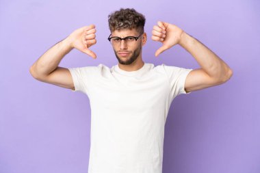 Mor arka planda izole edilmiş beyaz bir adam baş parmağını iki eliyle aşağı gösteriyor.