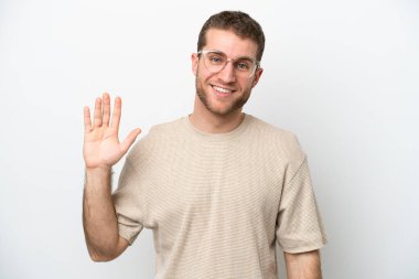 Beyaz arka planda izole edilmiş genç beyaz bir adam mutlu bir ifadeyle selamlıyor.