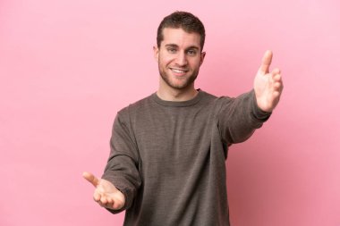 Pembe arka planda izole edilmiş genç beyaz adam sunar ve davet eder.