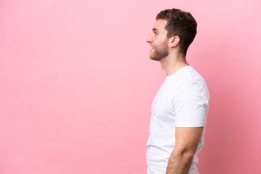 Pembe arka planda izole edilmiş genç beyaz adam yan yana gülüyor.