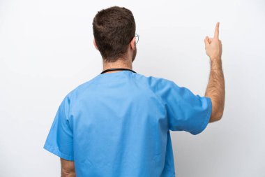 Young surgeon doctor caucasian man isolated on white background pointing back with the index finger