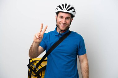 Beyaz arka planda izole edilmiş termal sırt çantalı beyaz adam gülümsüyor ve zafer işareti gösteriyor.