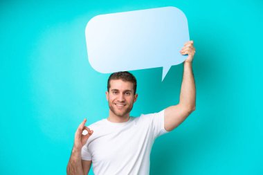 Beyaz, mavi arka planda izole edilmiş genç bir adam elinde boş bir konuşma balonu tutuyor ve 