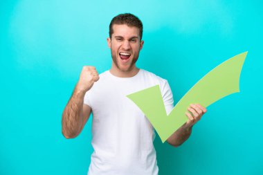 Mavi arka planda izole edilmiş genç beyaz bir adam elinde bir çek ikonu tutuyor ve zaferi kutluyor.