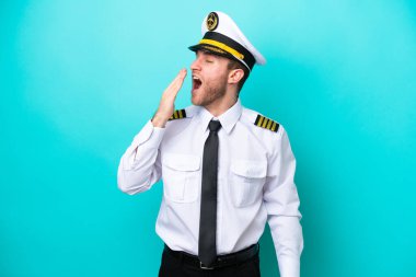 Airplane caucasian pilot isolated on blue background yawning and covering wide open mouth with hand