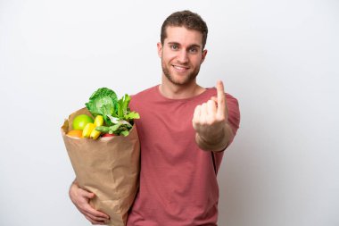 Young caucasian man holding a grocery shopping bag isolated on white background doing coming gesture