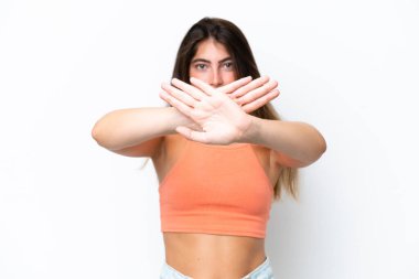 Beyaz arka planda izole edilmiş genç beyaz bir kadın bir eylemi durdurmak için el hareketi yapıyor.