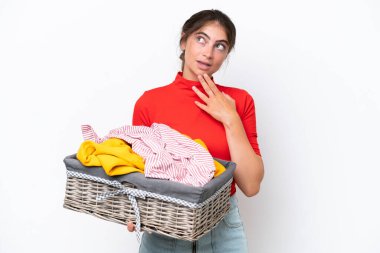 Young caucasian woman holding a clothes basket isolated on white background looking up while smiling