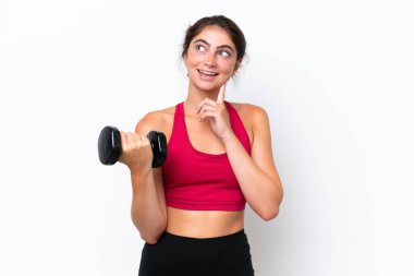 Beyaz arka planda ağırlık kaldıran beyaz saçlı genç bir kadın yukarı bakarken bir fikir düşünüyor.