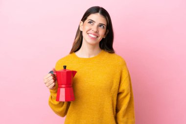 Young Italian woman holding a coffee maker isolated on pink background thinking an idea while looking up