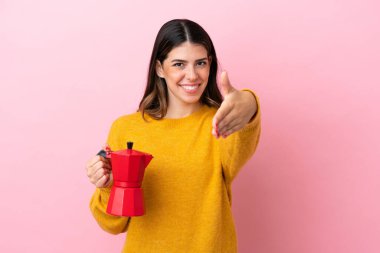 Young Italian woman holding a coffee maker isolated on pink background shaking hands for closing a good deal