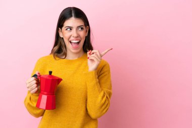 Young Italian woman holding a coffee maker isolated on pink background intending to realizes the solution while lifting a finger up