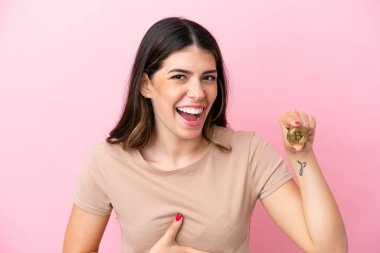 Pembe arka planda izole edilmiş Bitcoin tutan genç İtalyan kadın çok gülümsüyor.