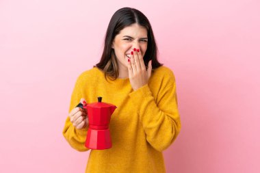Young Italian woman holding a coffee maker isolated on pink background happy and smiling covering mouth with hand