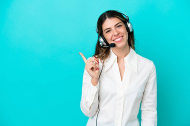 Telemarketer Italian woman working with a headset isolated on blue background pointing to the side to present a product