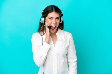 Telemarketer Italian woman working with a headset isolated on blue background with surprise and shocked facial expression
