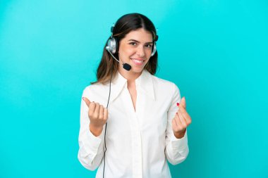 Telemarketer Italian woman working with a headset isolated on blue background making money gesture