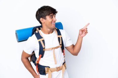 İzole edilmiş beyaz arka planda büyük bir sırt çantasıyla genç dağcı kadın parmak göstererek bir ürün sunuyor.