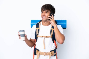 İzole edilmiş beyaz arka planda büyük bir sırt çantasıyla genç dağcı kadın elinde kahve ve bir cep telefonu tutuyor.