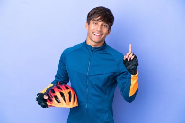 Young cyclist caucasian man isolated on purple background showing and lifting a finger in sign of the best
