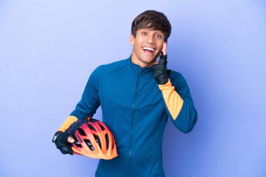 Young cyclist caucasian man isolated on purple background with surprise and shocked facial expression