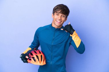 Young cyclist caucasian man isolated on purple background making phone gesture. Call me back sign