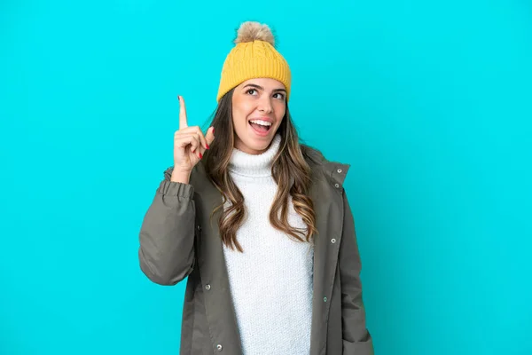 Young Italian woman wearing winter jacket and hat isolated on blue background intending to realizes the solution while lifting a finger up